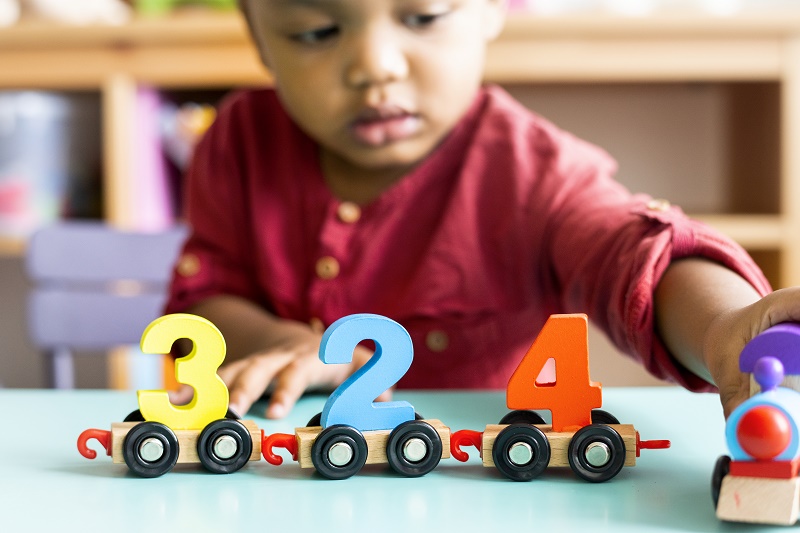 Young boy of color playing with a wooden train carrying number blocks.